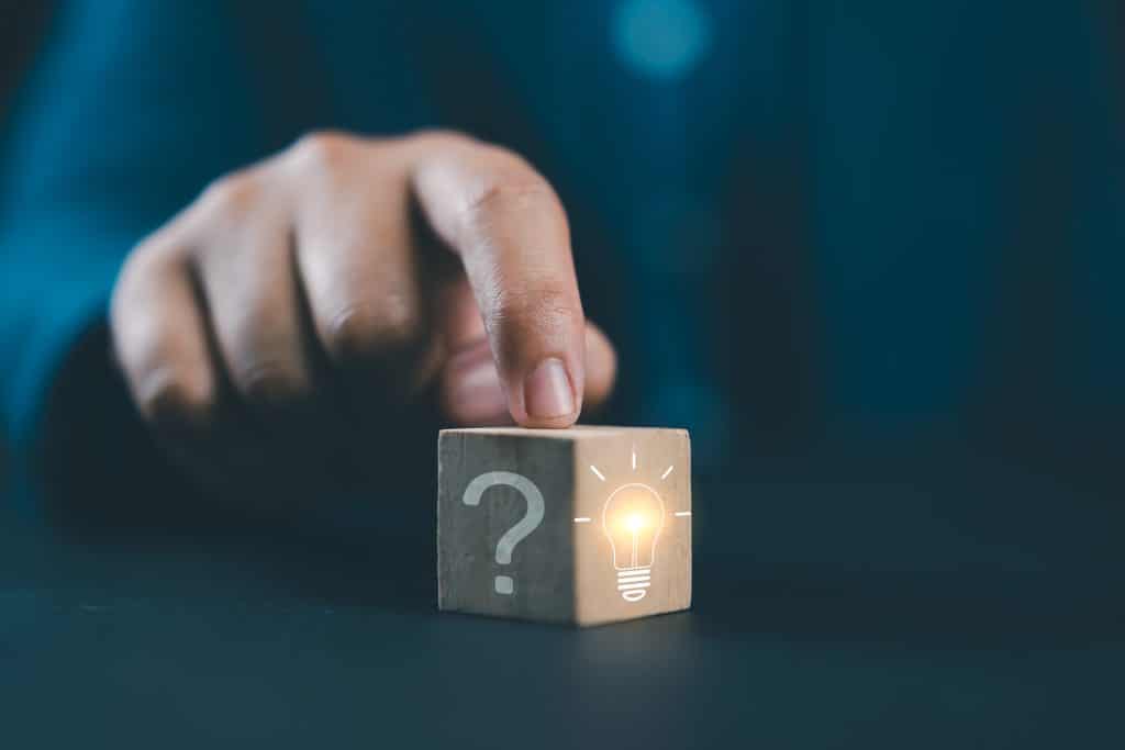 Hand touching Glowing light bulb on bright side and question mark on dark side of wooden block cube for problem solving solution and creative thinking idea innovation concept.